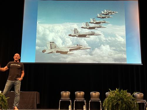 Pilot John Foley on stage with jets in formation behind him